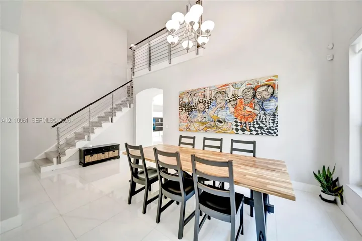 High-ceilinged room featuring large-format tile flooring, a multi-globe chandelier, and an open staircase with a metal cable railing system