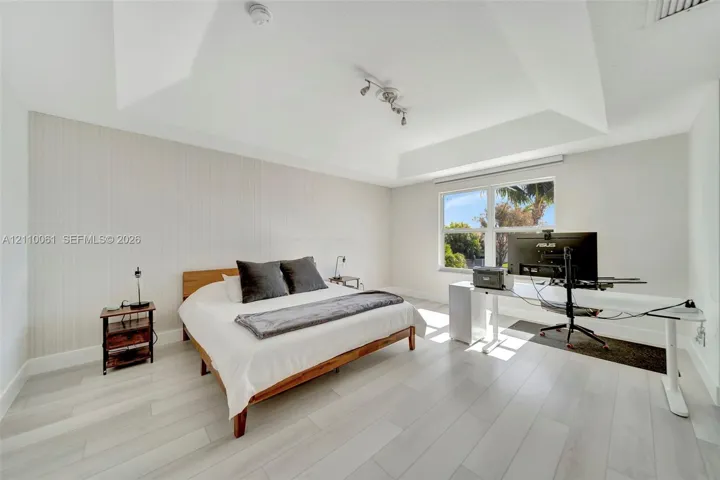Tray ceiling, vertical panel accent wall, light-toned wood-finish flooring, and multi-pane window