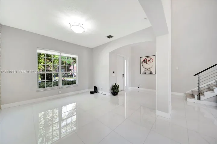 High-gloss tile flooring, arched architectural opening, multi-pane window, and staircase featuring a metal railing system