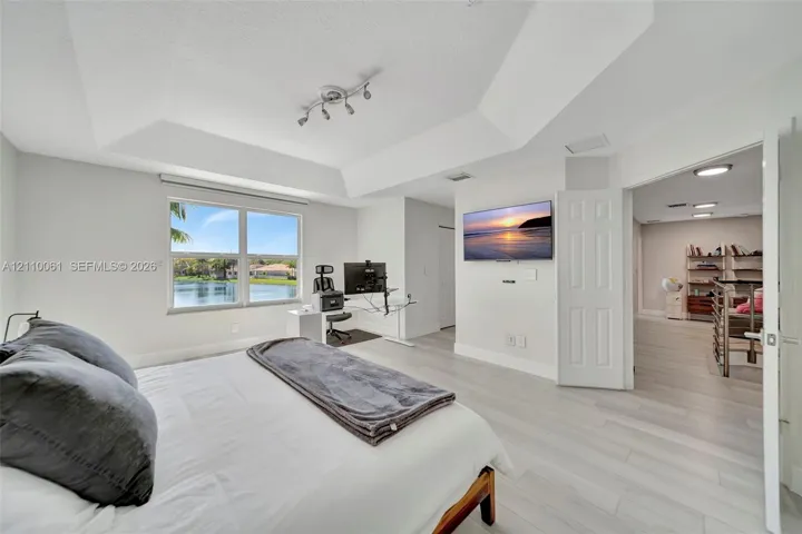 Tray ceiling with multi-directional track lighting, light-toned wood-finish flooring, and large window with water exposure