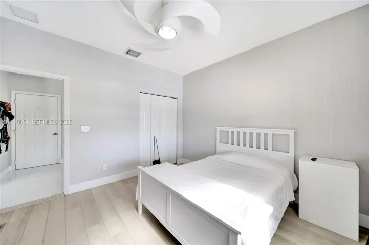 Room featuring wood-finish flooring, textured wall covering, bi-fold closet doors, and a multi-blade ceiling fan with integrated lighting