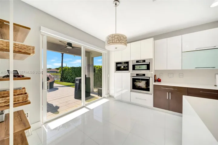 Kitchen featuring high-gloss white cabinetry, dual-tone lower storage, built-in stainless steel double wall ovens, large-format tile flooring, and sliding glass doors