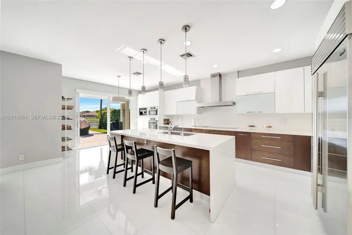 Contemporary kitchen featuring an expansive waterfall-edge island, two-tone cabinetry with gloss-finish uppers, stainless steel professional-grade appliances, recessed lighting, and large-format tile flooring