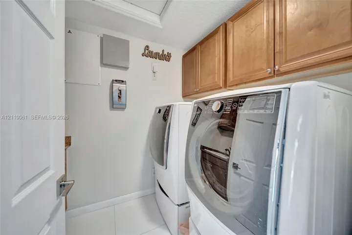 Dedicated laundry area featuring upper wood cabinetry and white tiled flooring