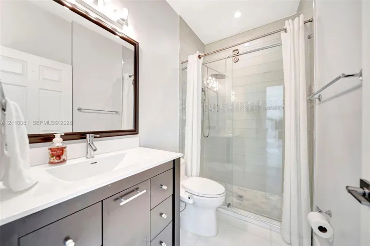 Bathroom featuring a dark-finish vanity with a rectangular sink, quartz countertop, framed wall mirror, and a walk-in shower with sliding glass doors and tiled​​‌​​​​‌​​‌‌​‌‌​​​‌‌​‌​‌​‌​​​‌​​ surround