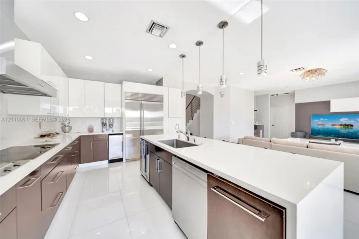 Kitchen featuring high-gloss white and dual-tone cabinetry, expansive solid-surface island, stainless steel appliances, and polished tile flooring