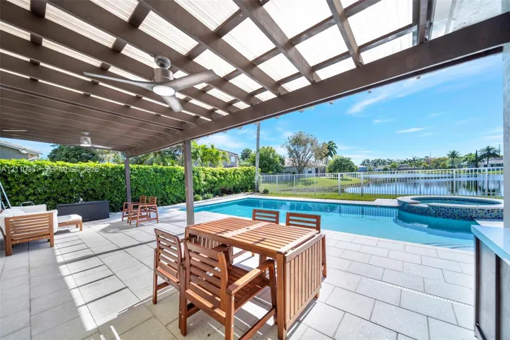Covered patio featuring a wood-beam pergola, integrated ceiling fans, stone paver flooring, an in-ground pool, and a raised spillover spa