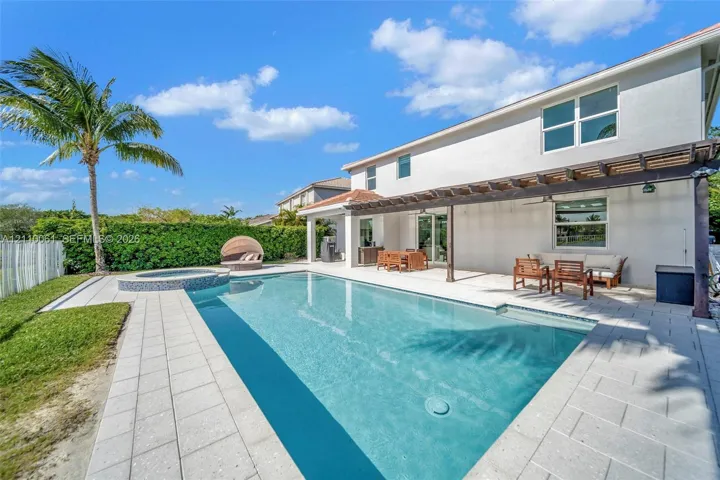 Backyard featuring a custom swimming pool, a raised tiled spa, a covered pergola, and paved decking