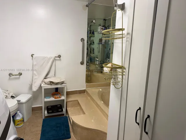 Full-height built-in cabinetry with matte black hardware, sunken soaking tub with integrated surround, floor-to-ceiling mirror, and wall-mounted support bars