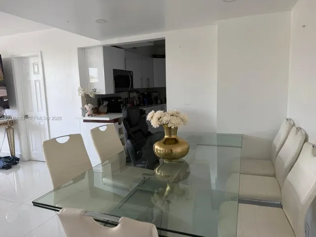 Dining area featuring high-gloss tile flooring, recessed ceiling lighting, and a neutral color palette, opening to a kitchen equipped with white cabinetry and a built-in microwave