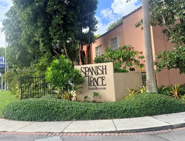 Stucco monument signage featuring professional lettering, complemented by mature landscaping, palm trees, and a decorative black iron perimeter fence