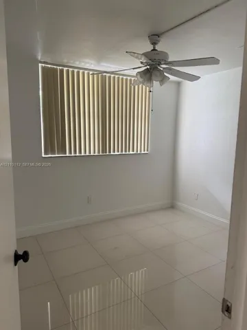 Neutral interior space featuring large-format tile flooring, white wall finishes, a ceiling-mounted light fixture with fan, and vertical window blinds