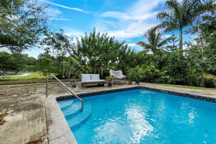 In-ground pool featuring a metal handrail, concrete patio surround, mature trees, and perimeter fencing