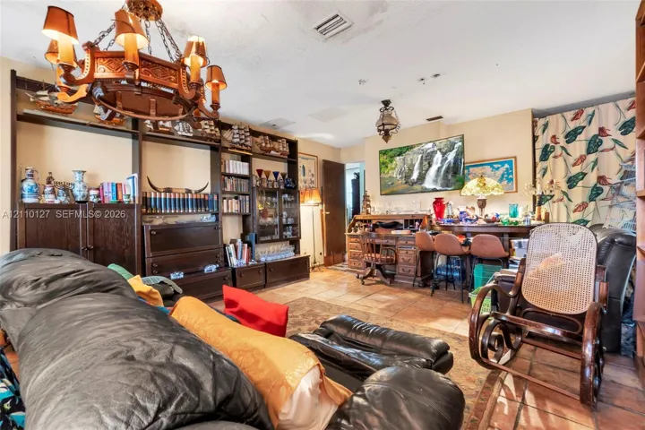 Living space featuring floor-to-ceiling dark wood built-in cabinetry, ornate metal chandelier, and terracotta-toned tile flooring