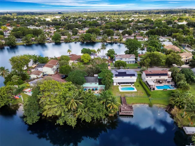 Waterfront residential setting featuring a private dock, swimming pools, mature landscaping, and solar panel arrays