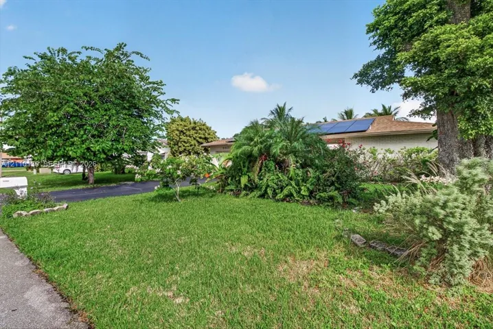 Exterior featuring a pitched roof with integrated solar panels, mature landscaping, and a paved driveway