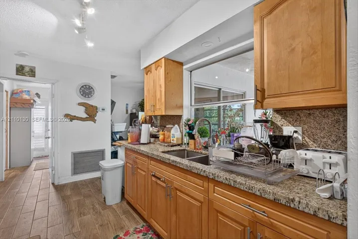 Kitchen featuring natural wood cabinetry, stone-finish countertops, dual-basin stainless steel sink with a high-arch pull-down faucet, and wood-finish tile flooring