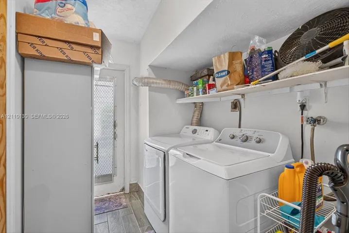 Laundry area featuring wood-finish tile flooring, white-finish wall-mounted shelving, and a metal-frame exterior door