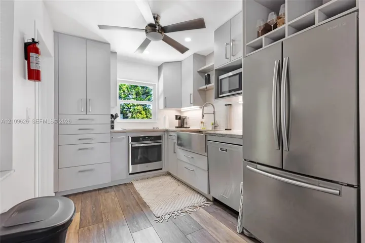 Kitchen featuring light gray cabinetry, stainless steel appliances, a farmhouse-style sink, wood-finish flooring, and a ceiling fan with integrated lighting