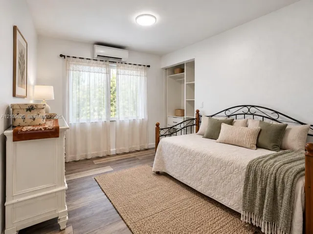 Wood-finish flooring, wall-mounted climate control unit, built-in shelving, and flush-mount ceiling lighting