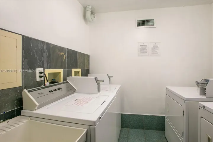 Laundry area featuring tile flooring, stone wall backsplash, and a utility sink