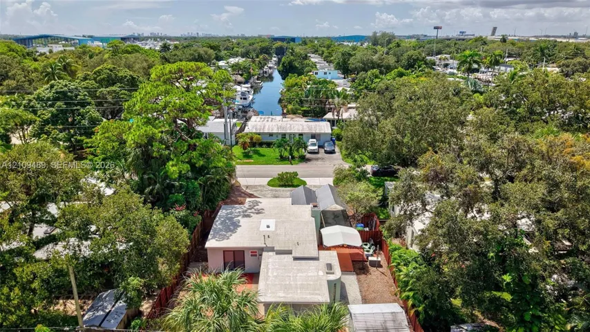 Aerial perspective of property featuring a flat roofline, paved driveway, enclosed rear outdoor area, and mature landscaping