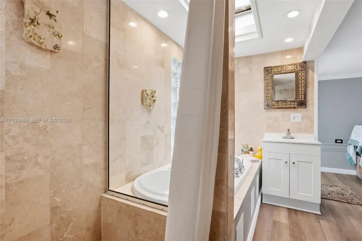 Bathroom featuring stone tile walls, a built-in soaking tub, a skylight, wood-finish flooring, and a white vanity cabinet