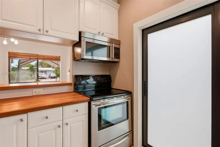 Kitchen featuring white shaker-style cabinetry, stainless steel microwave, black electric range, wood countertop, and a sliding glass door with a dark frame