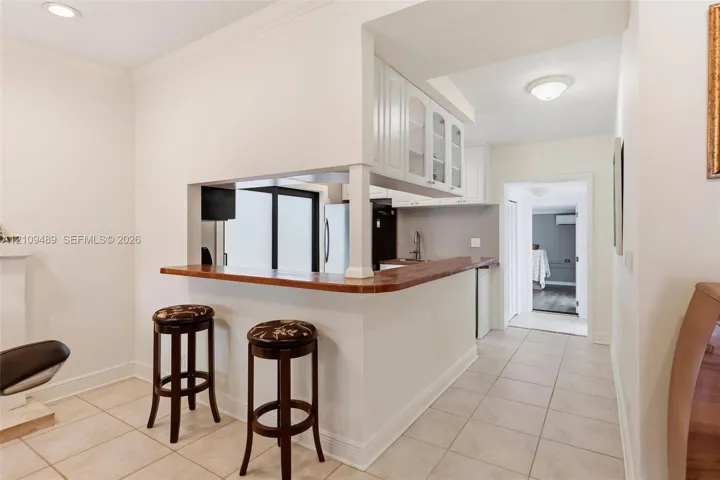 Pass-through kitchen counter with wood surface, white cabinetry with glass-front uppers, and neutral tile flooring