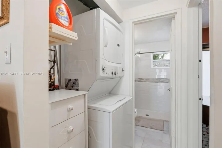 Stacked laundry unit with built-in storage cabinetry, white tile bathroom flooring, subway tile shower surround, and a framed window