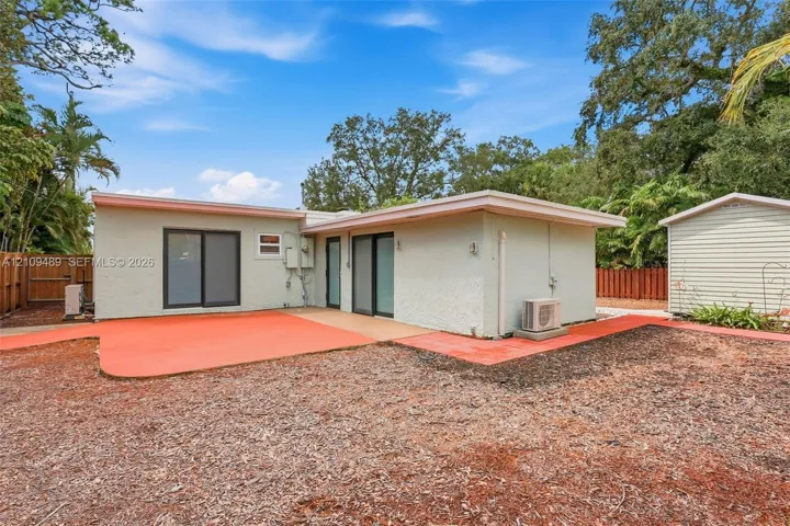 Stucco exterior featuring dual sliding glass doors, a painted concrete patio, and a detached storage structure enclosed by perimeter wood fencing