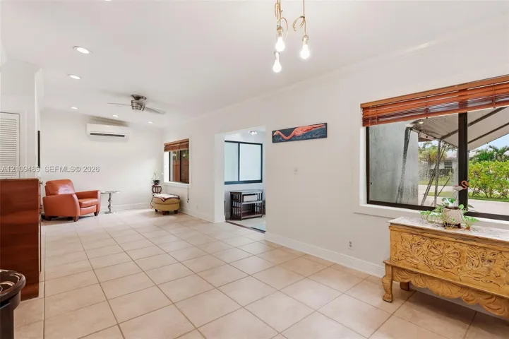 Tile flooring, recessed lighting, wall-mounted climate control unit, crown molding, and large-paned windows with wood-slat blinds