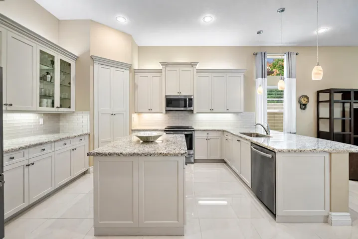 Kitchen featuring light-toned cabinetry, stone-surface countertops, central island, tiled backsplash, and stainless-steel appliances