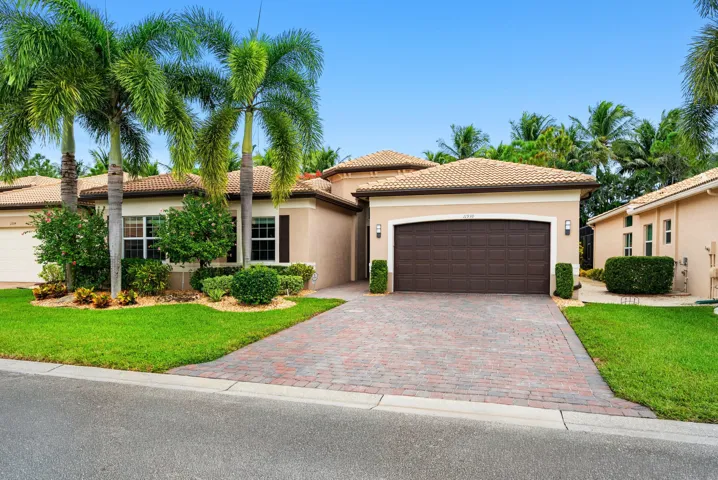 Stucco exterior residence featuring a multi-hipped tile roof, paver driveway, arched garage entry, and mature palm landscaping