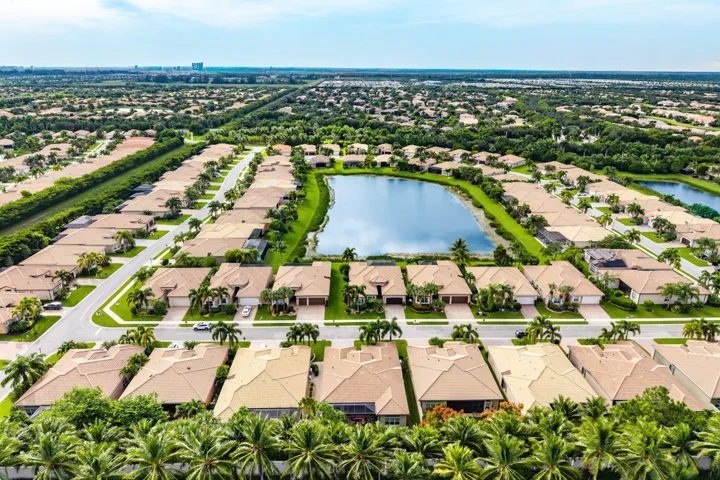 Aerial perspective of a residential community centered around a large lake, featuring multiple tile-roof homes, paved street infrastructure, and established landscaping