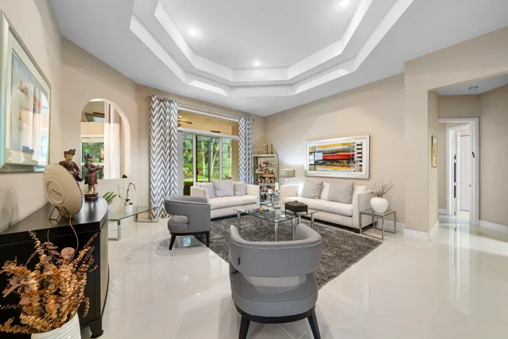 Tray ceiling with recessed lighting, large-format tile flooring, arched wall cutout, and sliding glass doors
