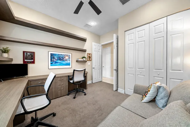 Built-in desk with integrated drawer storage, custom floating shelves, ceiling fan, and floor-to-ceiling bi-fold closet doors