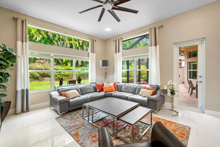 High-ceilinged living area featuring expansive windows with transom glass, large-format tile flooring, and a ceiling fan