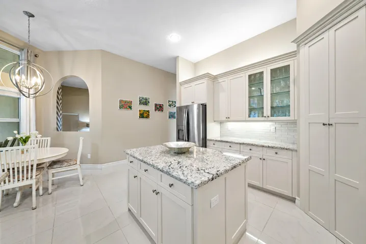 Kitchen featuring custom cabinetry with glass-front display uppers, a central island with stone countertop, stainless steel refrigerator, and tiled flooring