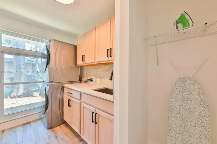 Utility room featuring light-finish cabinetry, a white countertop with an integrated sink, a ceramic tile backsplash, and wood-finish flooring