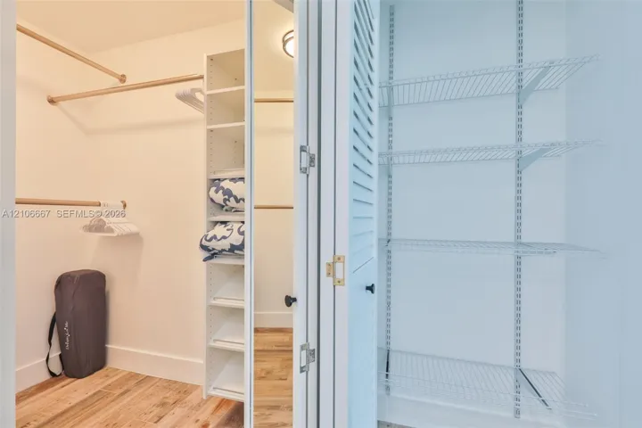 Walk-in closet featuring wood-finish flooring, built-in shelving tower, tiered hanging rods, and a separate pantry-style storage area with louvered doors and wire shelving
