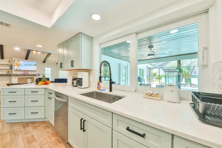 Kitchen featuring light-toned shaker cabinetry, quartz countertops, stainless steel undermount sink with matte black faucet, and wood-finish flooring