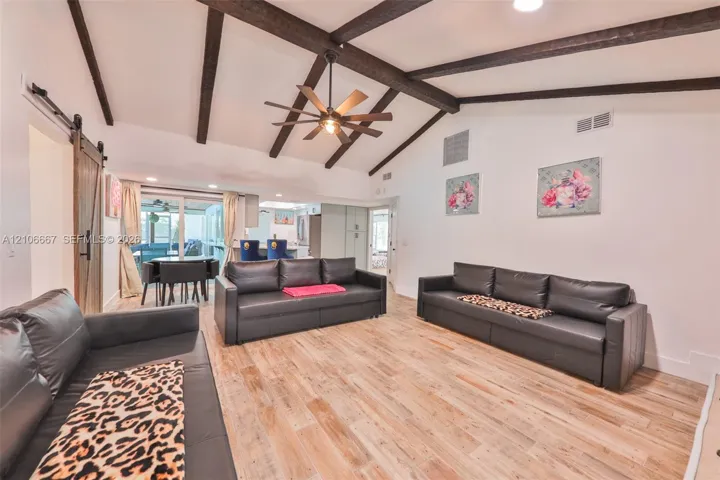 Vaulted ceiling featuring exposed decorative wooden beams, wood-finish flooring, and a central ceiling fan with an integrated light fixture