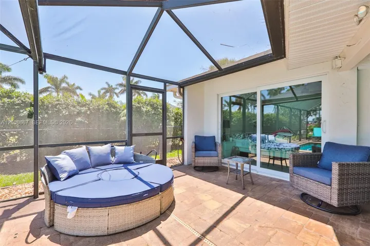 Screened-in lanai featuring paver flooring, a dark-frame enclosure, and large glass sliding doors