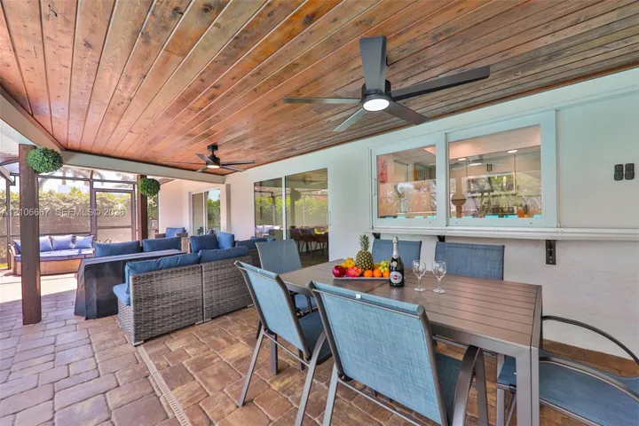 Covered patio featuring a wood-plank ceiling, paver flooring, dual ceiling fans, and an exterior pass-through window
