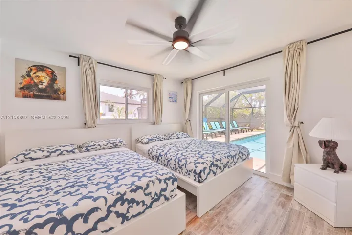 Room featuring wood-finish flooring, a multi-blade ceiling fan with integrated lighting, and sliding glass doors providing access to a screened-in pool enclosure
