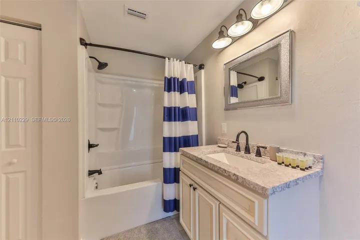 Vanity featuring a stone-composite countertop, integrated rectangular sink, oil-rubbed bronze faucet, and shaker-style cabinetry, complemented by a tub-shower combination with matching bronze fixtures and a three-light vanity fixture