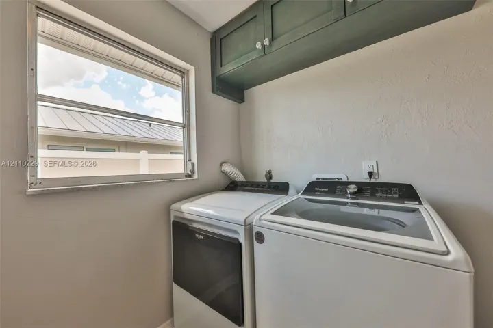 Laundry area featuring dark-finished upper cabinetry, a single-pane window, and white finish laundry appliances