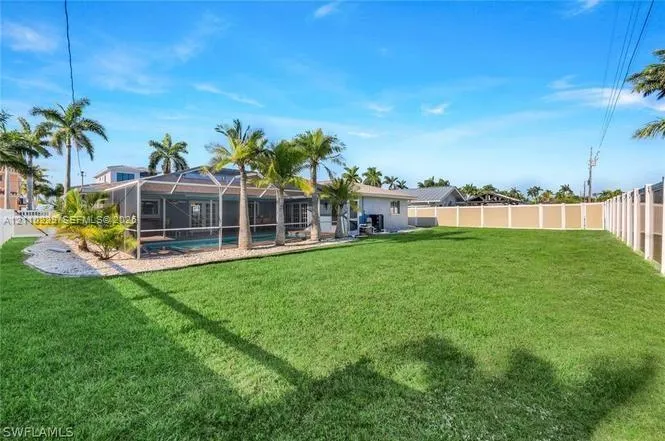 Expansive backyard featuring a manicured lawn, full-height privacy fencing, a screen-enclosed pool, and integrated landscape palms