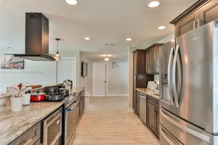 Kitchen featuring stone countertops, stainless steel appliances, dark wood cabinetry, recessed lighting, and tile flooring